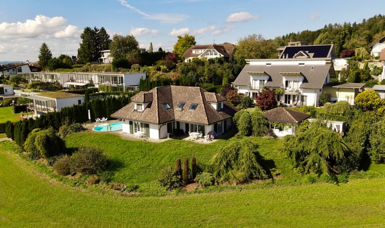 Drohnenaufnahme eines Einfamilienhauses mit Garten, Pool und umliegender Wohngegend