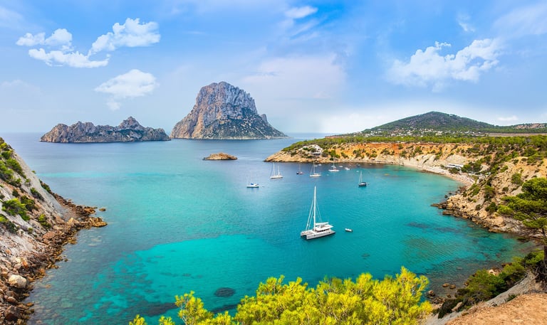 Sailboats in water with rock formation off the coast of Ibiza Spain