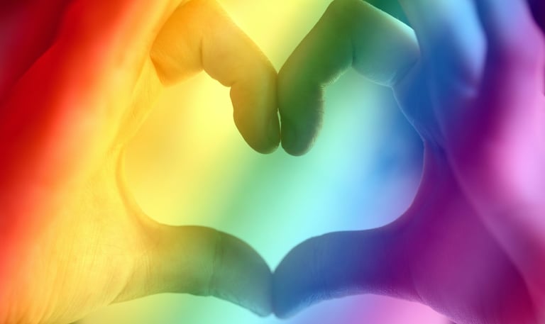 holding hands in a heart shape with a pride rainbow background