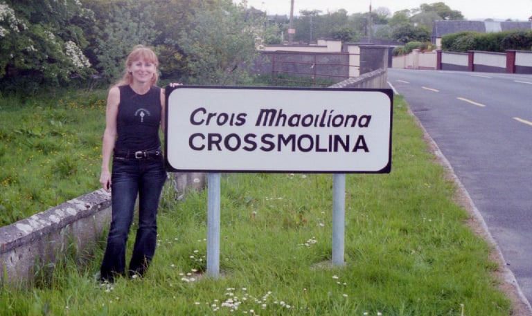 Annie of Crossmolina Band standing next to the welcome sign, County Mayo, Republic of Ireland.