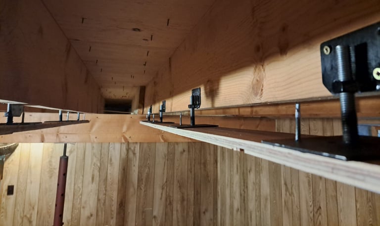 Adjustable metal brackets installed between wood joists for precision ceiling levelling in basement renovation