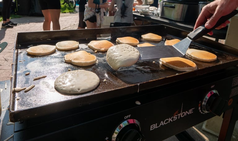 A hand flipping pancakes with a spatula, with people in the background