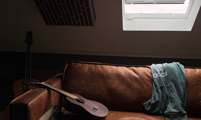Guitar resting on leather couch under roof window in studio room