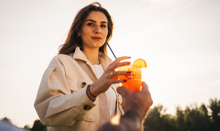 Frau greift bei Sonnenuntergang nach einem Cocktailglas – warmer Lichtmoment, filmische, ruhig