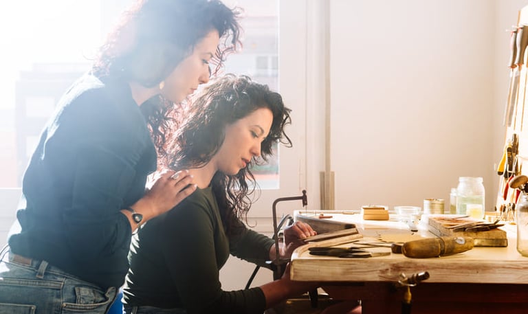 Dos artesanas elaborando joyería hecha a mano en una mesa de trabajo luminosa dentro de un taller.