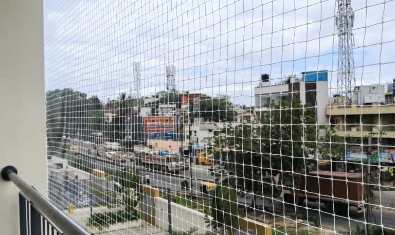 A balcony in AElectronic City fitted with a sturdy cat safety net, sunlight filtering through.