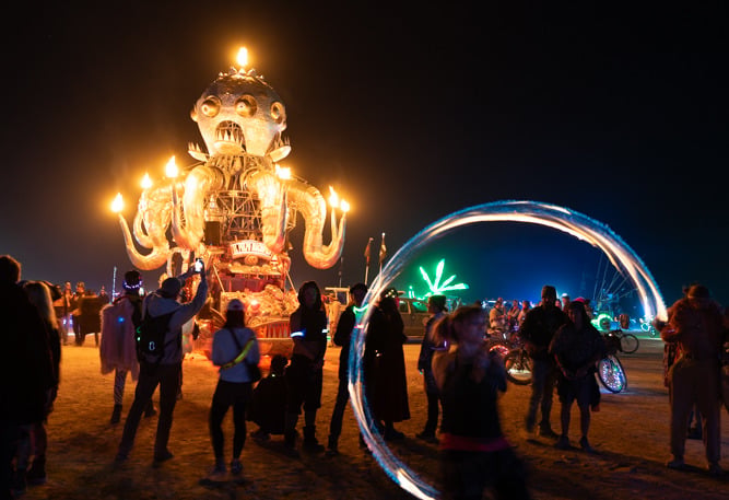 A fire-breathing octopus art car and light dancers in the desert night.