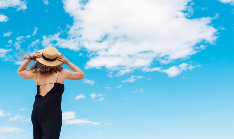 Mulher com chapéu de costas olhando o céu azul