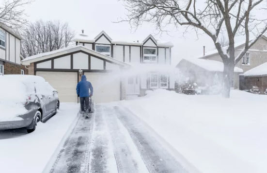 a person using a snow blower to clear snow from the driveway
