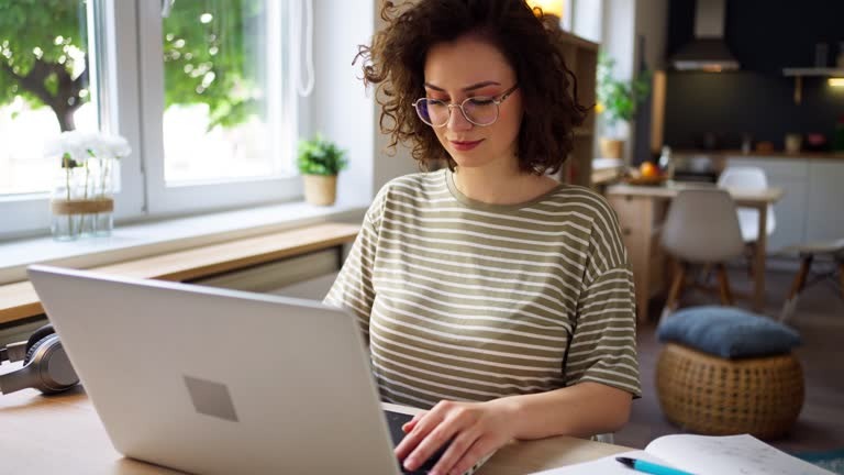 uma mulher de óculos, cabelos ondulados, mexendo em um notebook