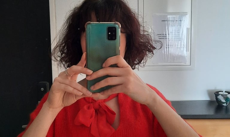 Selfie allo specchio con top rosso e smartphone verde che copre il volto