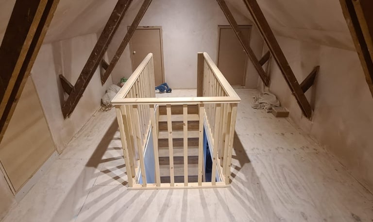 Unfinished attic conversion featuring a new wooden staircase banister and plywood flooring in a loft space.