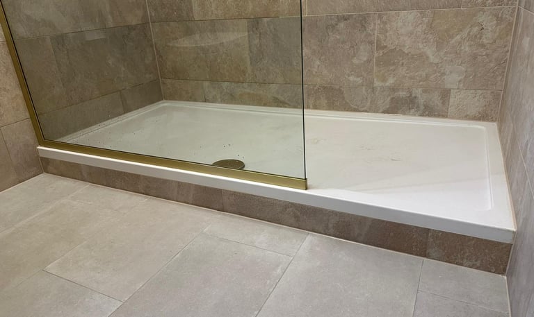 Walk-in shower with a low-profile white tray, glass enclosure, and beige stone wall tiles.