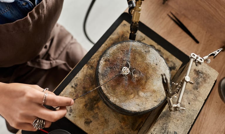 Joyero usando un soplete para soldar un anillo de plata sobre un bloque de soldadura en un taller.