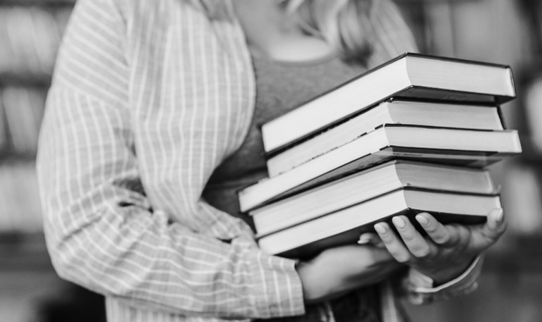 Kobieta w rękach trzyma stos książek.