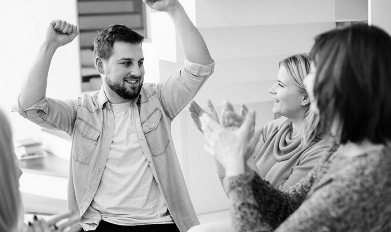 Mężczyzna unosi ręcę w górę, obok dwie kobiety biją brawo.