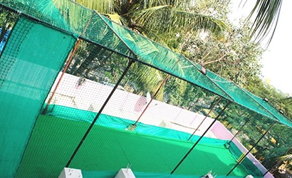 Workers carefully fitting a green safety net around a school rooftop sports area with city buildings