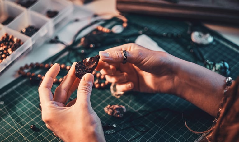 Manos artesanas inspeccionando una piedra natural oscura durante el proceso de joyería artesanal