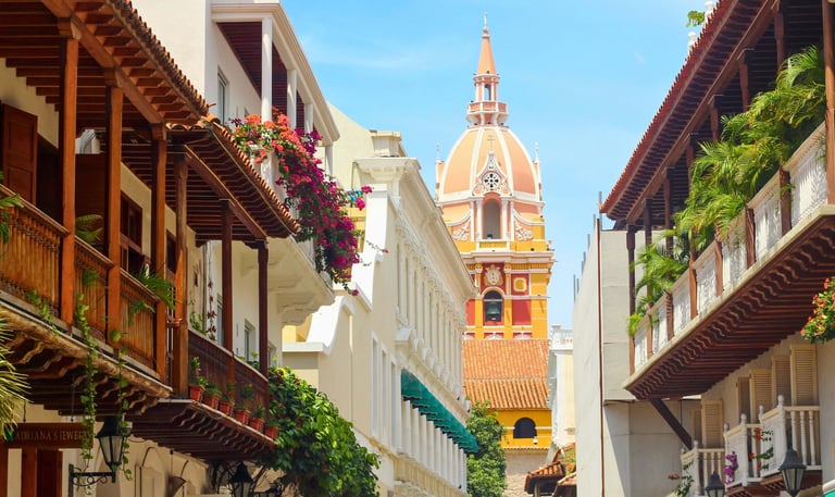 Historic street in Cartagena with colorful colonial architecture and the Santa Catalina Cathedral dome.
