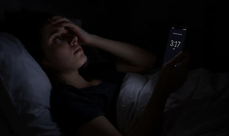A woman struggling with insomnia looks at her smartphone clock at 3:17 AM in a dark bedroom.