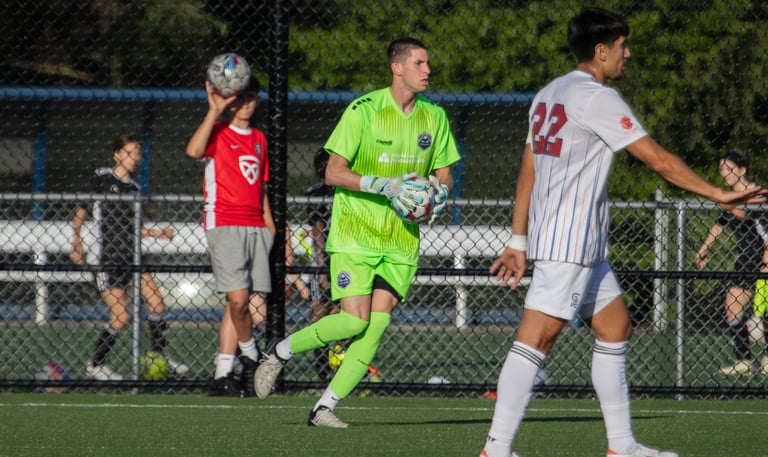 Midlakes goalkeeper with ball in hand looking to play it. Opposing player in foreground.