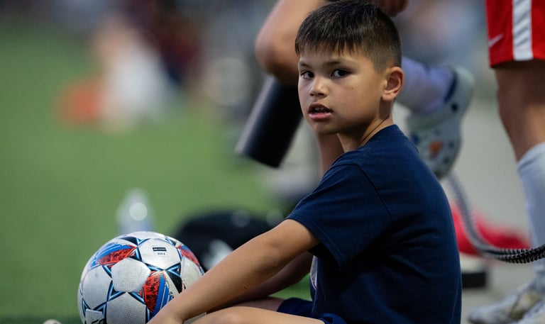 Ball boy sitting with a soccer ball.