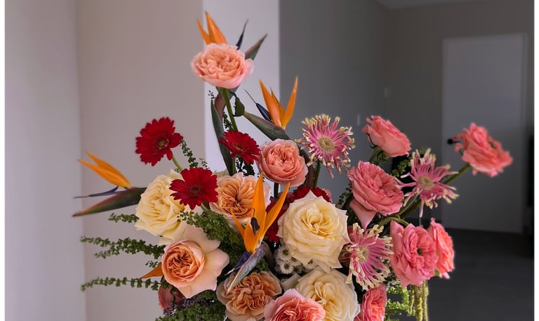A colorful flower arrangement with peach roses, red gerbera daisies, and orange bird of paradise stems.