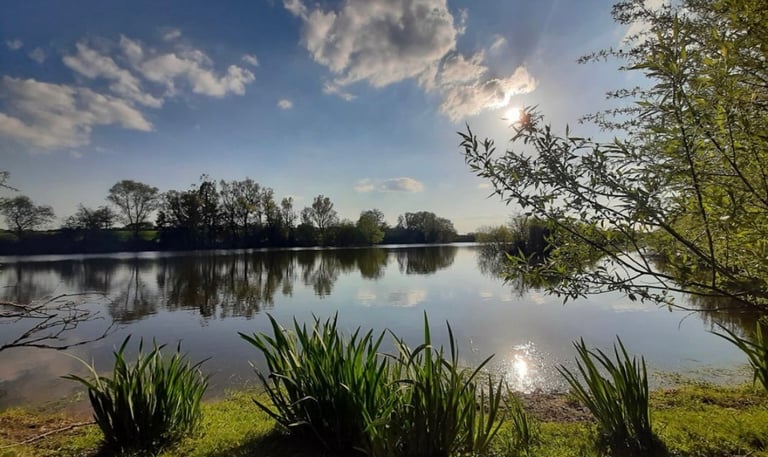 a lake with a sun shining through the clouds