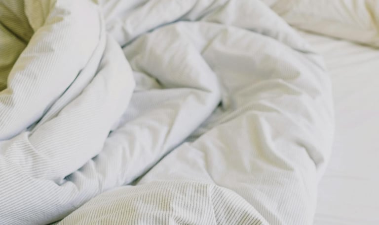A bed that is not made up with a disheveled white duvet and four white pillows