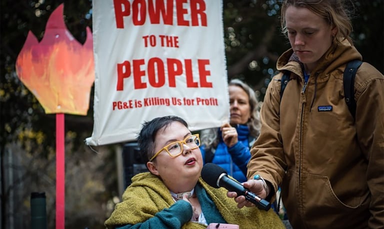 Photo of Stacey at a protest with sign that reads "power to the people PG&E is killing us for profit"