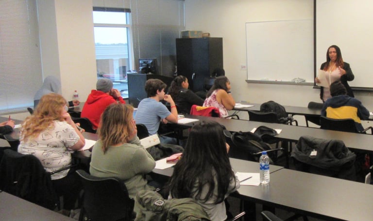 A diverse group of students in a classroom listening to a female teacher giving a lecture.