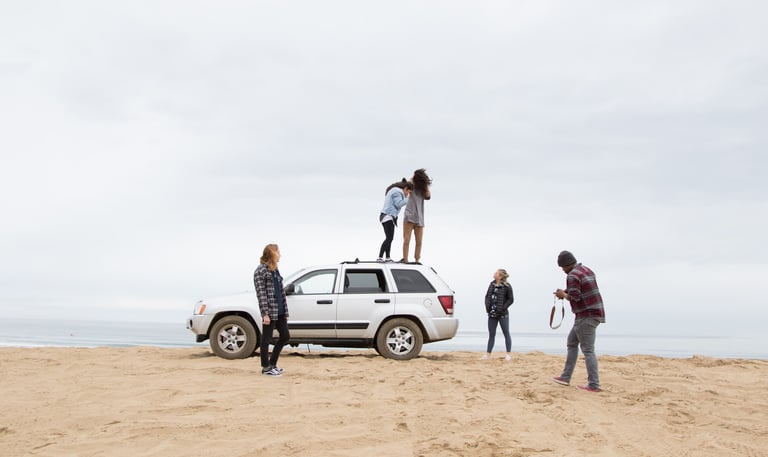 A group of friend in a beach. A car is parked on the beach and the group is posing for a picture