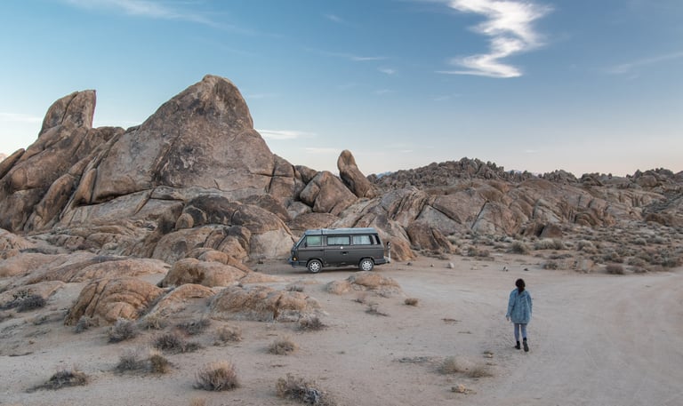 A rocky background with a van parked in the middle. A person seems to be walking towards the van.