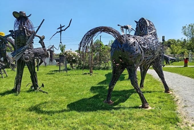 Handcrafted scrap metal sculptures of a horse and cowboy standing in an outdoor art garden.