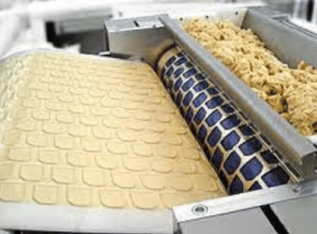 Industrial biscuit rotary moulder machine processing dough on a conveyor belt.