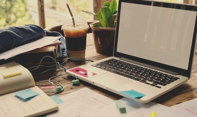 An aesthetic overhead shot of a home office desk with a laptop, iced coffee, plant, and notebook, creating a productive