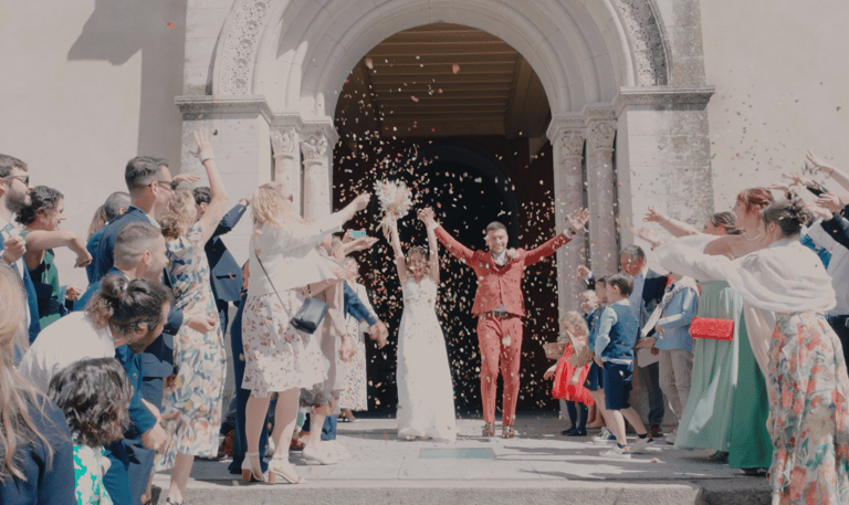 Des nouveaux mariés sortent de l'église avec les invités qui jettent des confettis