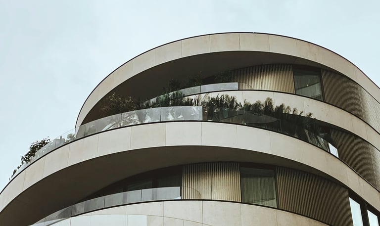 Edificio moderno, redondo, balcones con barandas de vidrio y revestimiento simil piedra y metal