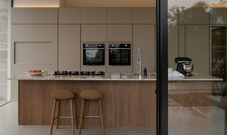 cocina moderna y calida, greige y madera, isla con bacha, anafe y desayunador. Heladera panelada.