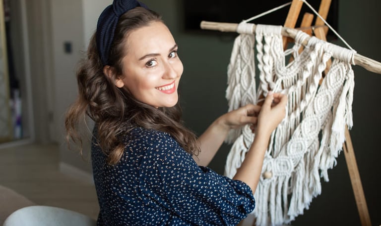 Una mujer sonriente creando un tapiz de macramé hecho a mano.