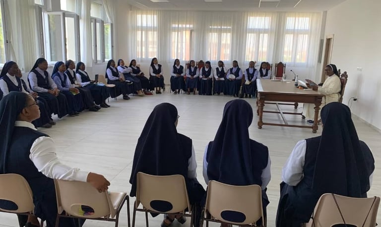 Catholic nuns in habits gather for a meeting in a bright seminar room with large windows.