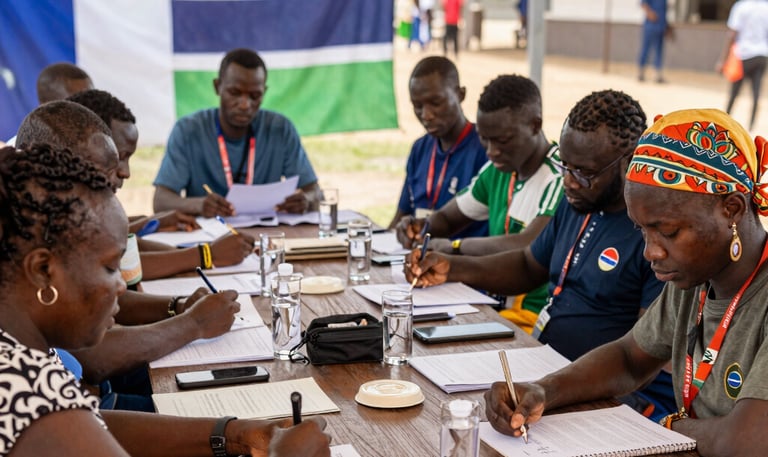 A group of Gambian and French professionals collaborating around a table with documents and laptops.