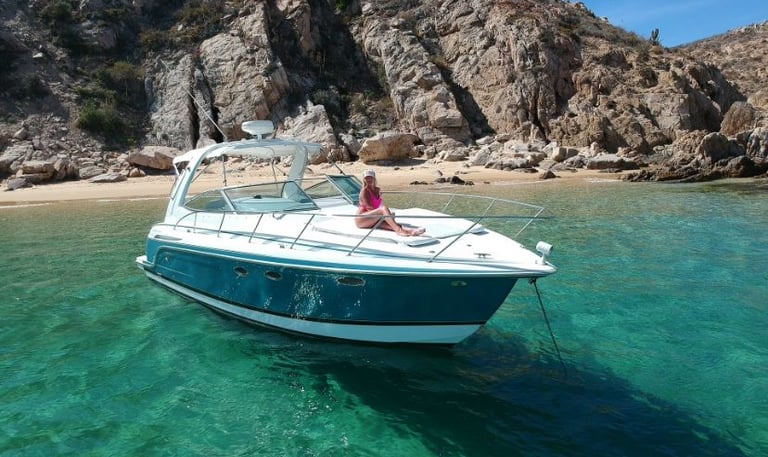 A luxury motorboat anchored in turquoise waters near a rocky coastline and sandy beach.
