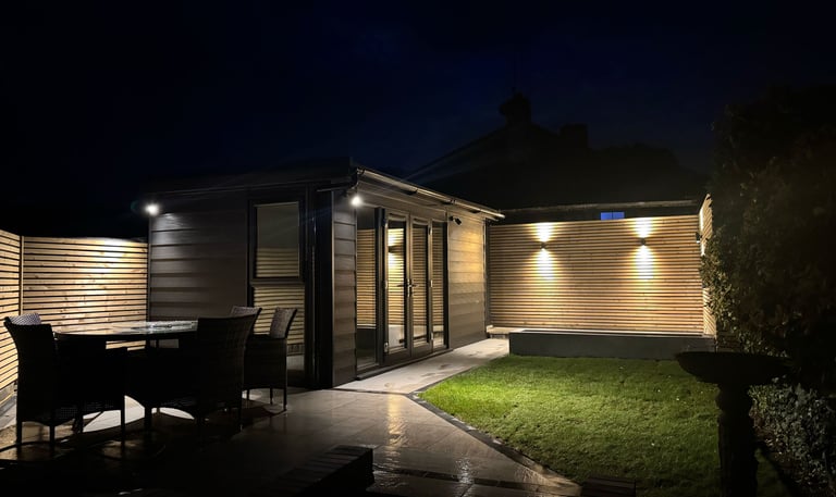 Modern garden room and patio with warm outdoor lighting and garden furniture at night.
