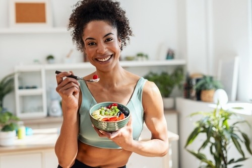 A smiling woman in fitness wear enjoying a healthy fruit and yogurt bowl for a nutritious breakfast.