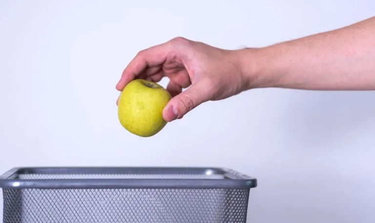 Hand tossing spoiled apple into trash can