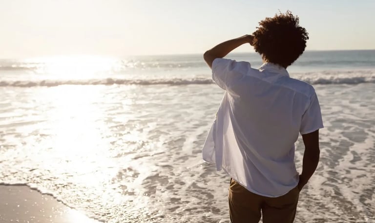 Un homme se tient debout sur la plage, contemplant l’horizon et les reflets du soleil sur l'océan.