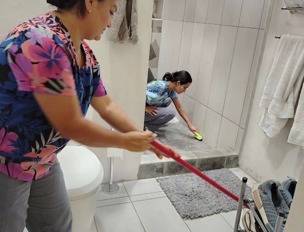 Professional cleaners scrubbing tile floors and shower walls in a modern bathroom.