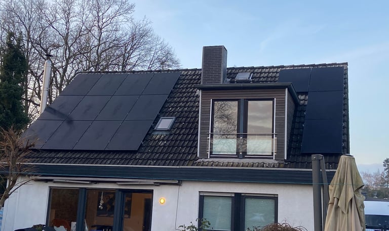 Modern house with black solar panels installed on a dark tiled roof next to a dormer window.