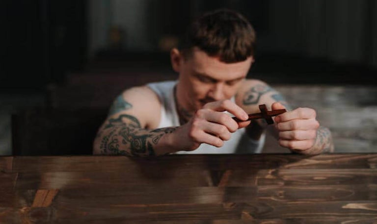 a man with tattoos on his arm, kneeling and holding a small cross